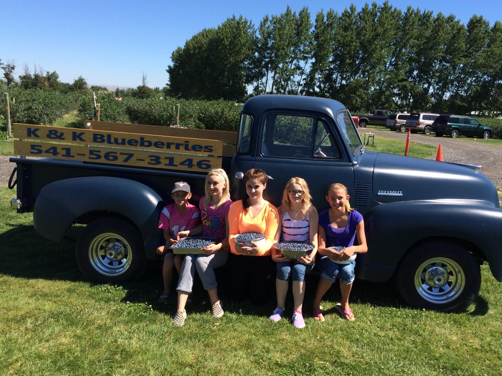 5 people hold trays of blueberries in front of an old chevy pickup