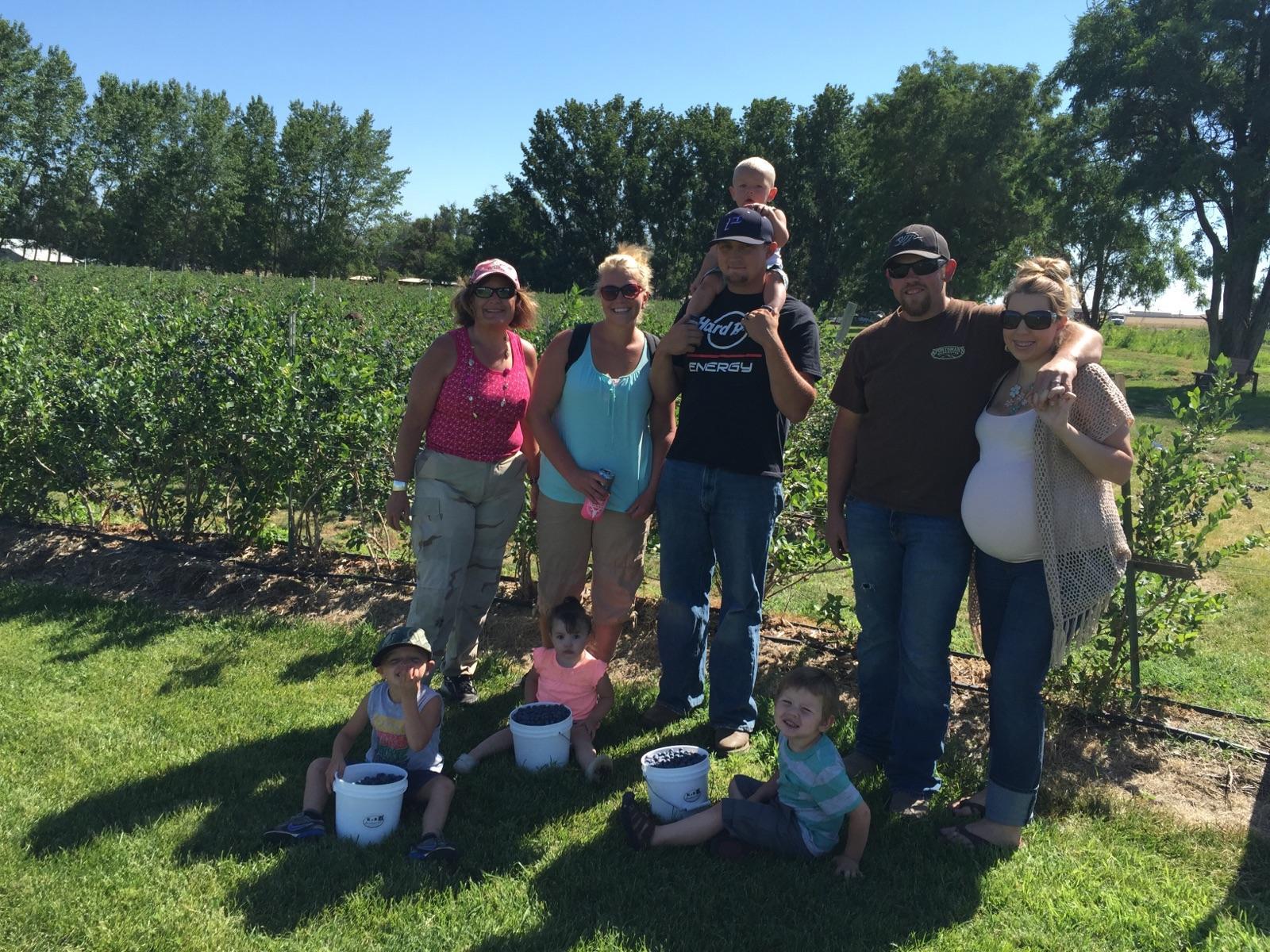 a group of people stand in front of a row of blueberries