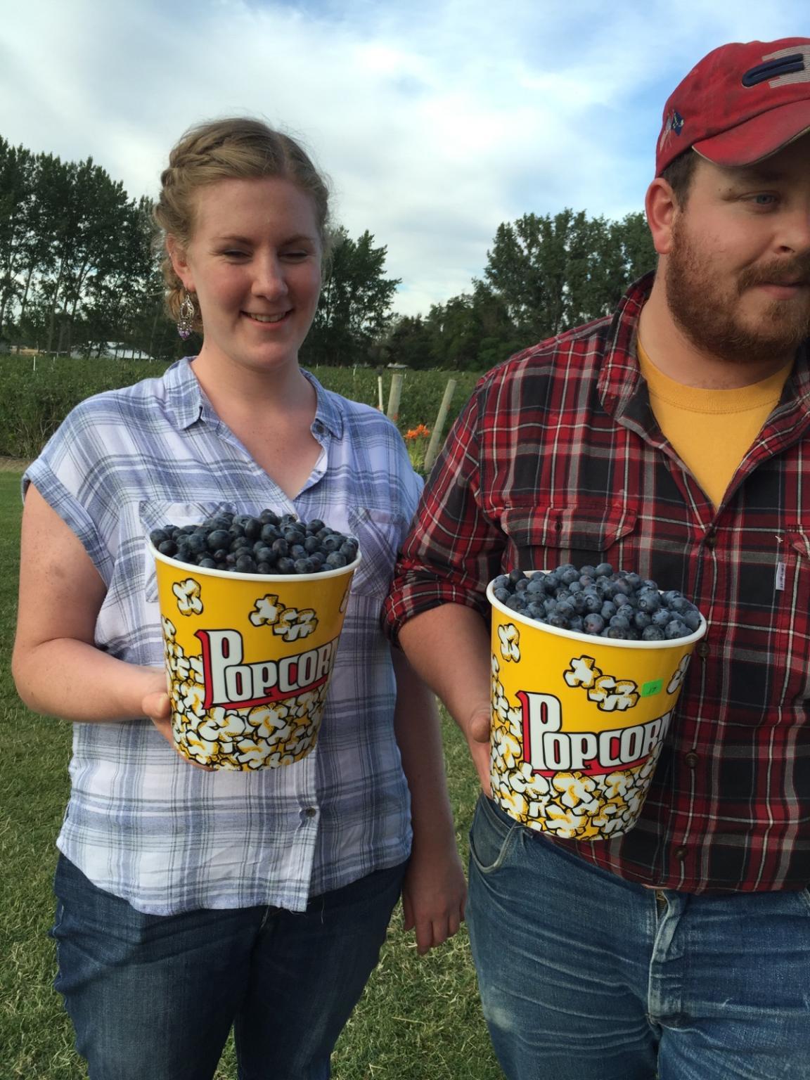 2 people carry popcorn bowls filled with blueberries