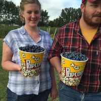 2 people carry popcorn bowls filled with blueberries
