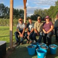 five people pose with large buckets of blueberries in front of them